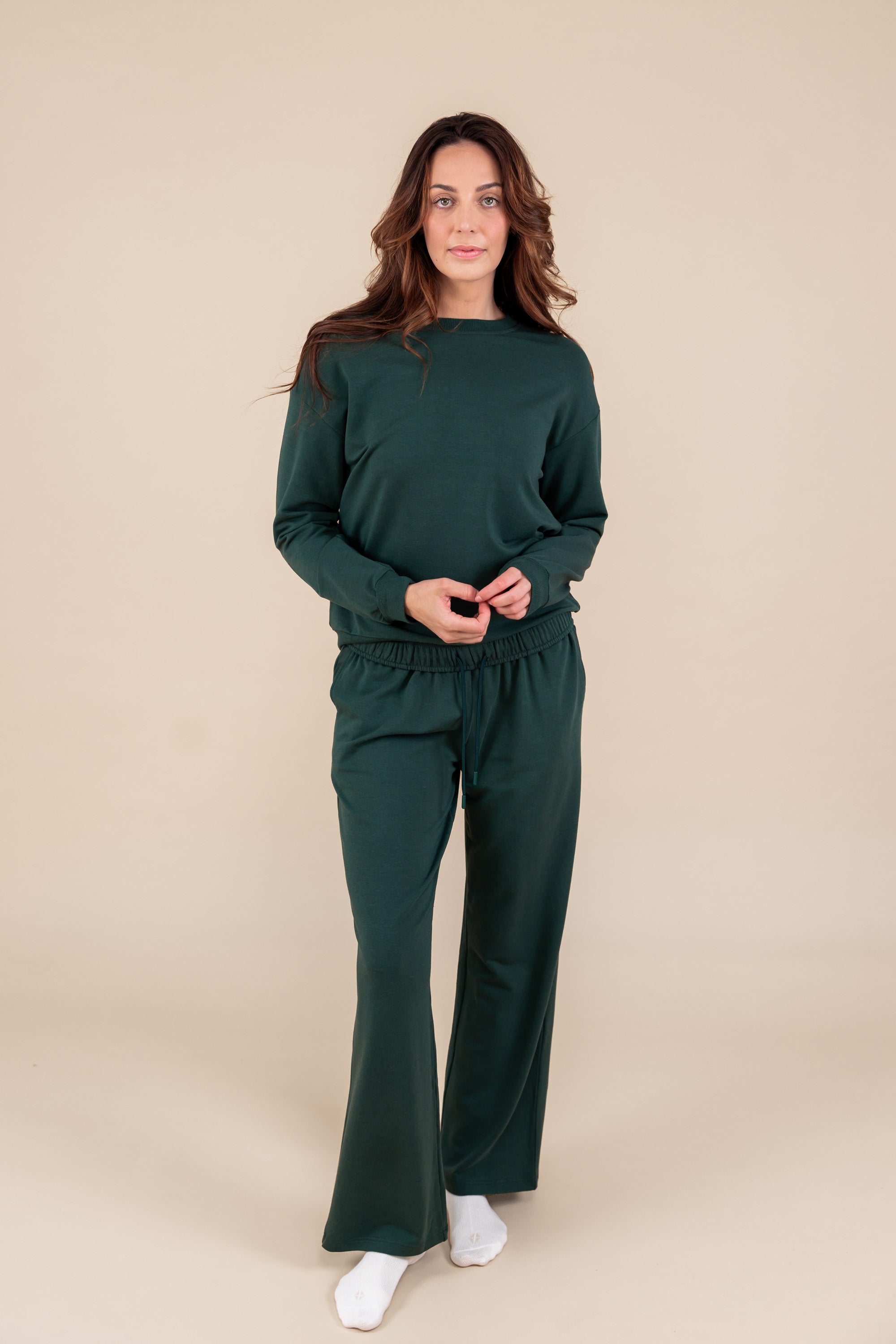 Woman wearing Women's Sweatpants in Cypress color under similar color women's sweatshirt on a beige background