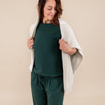 Woman wearing Women's Sweatpants in Cypress color under similar color women's sweatshirt and a beige sweater over her shoulders on a beige background