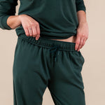 Close up of Modal wearing Women's Sweatpants in Cypress color under similar color women's sweatshirt on a beige background