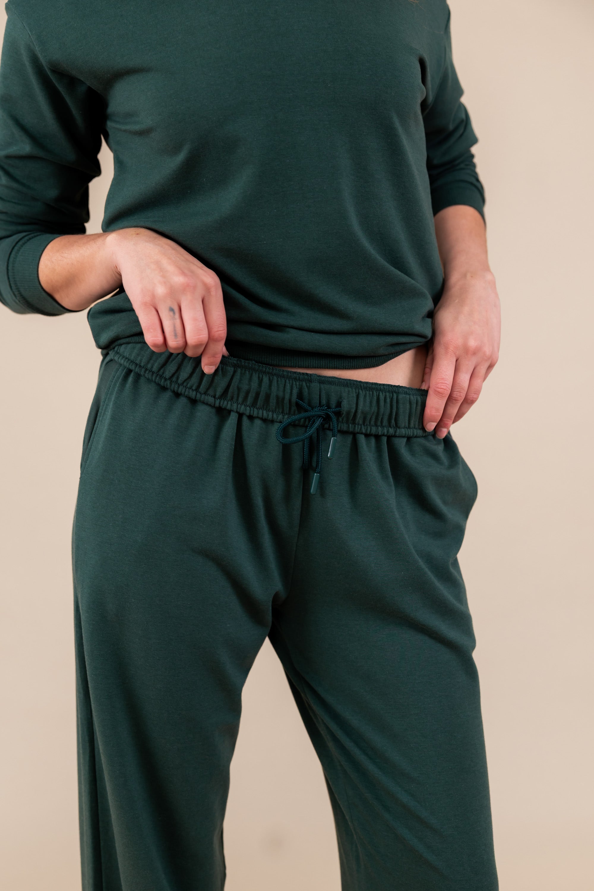 Close up of Modal wearing Women's Sweatpants in Cypress color under similar color women's sweatshirt on a beige background