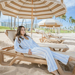 Woman relaxing on a beach chair under a large umbrella with palm trees and ocean in the background
