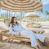 Woman relaxing on a beach chair under a large umbrella with palm trees and ocean in the background