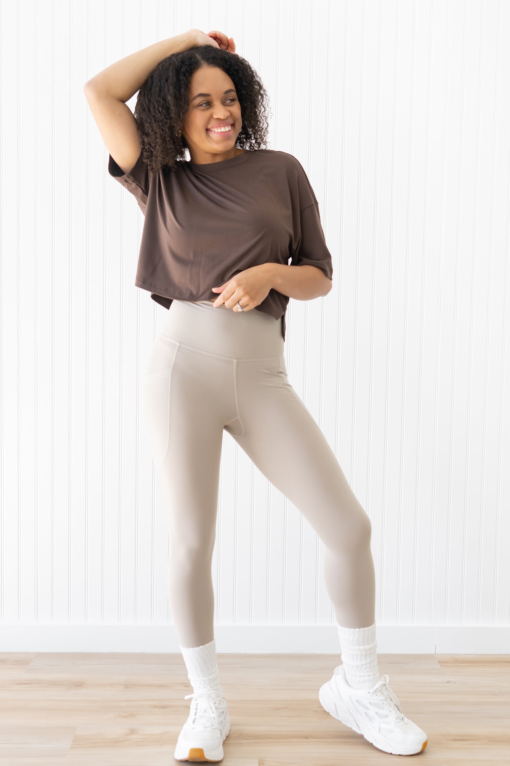Smiling model wearing the Flex Leggings in Bisque paired with a crop