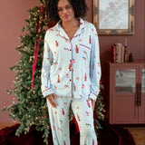 Woman wearing a blue pajama set with a festive print of santas, champagne, mugs, and disco balls standing in front of a christmas tree. 
---1605 3