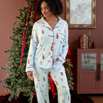 Woman wearing a blue pajama set with a festive print of santas, champagne, mugs, and disco balls standing in front of a christmas tree. 
::: Model is 5'6" wearing size M ///
---PJ 4