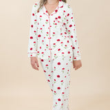 Woman wearing a white pajama set with red floral pattern on a beige background