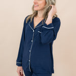 Woman wearing navy blue pajamas with white trim on a beige background