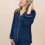 Woman wearing navy blue pajamas with white trim on a beige background