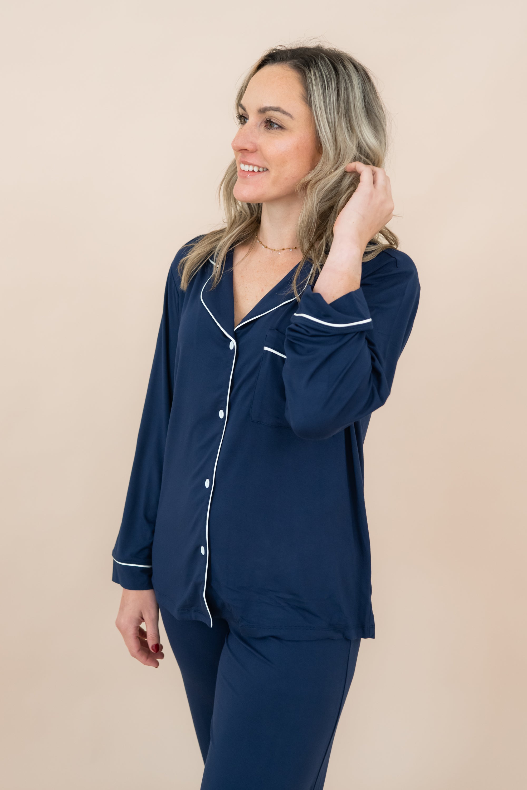 Woman wearing navy blue pajamas with white trim on a beige background