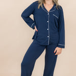 Woman wearing navy blue pajamas with white piping on a beige background