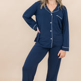 Woman wearing navy blue pajamas with white piping on a beige background