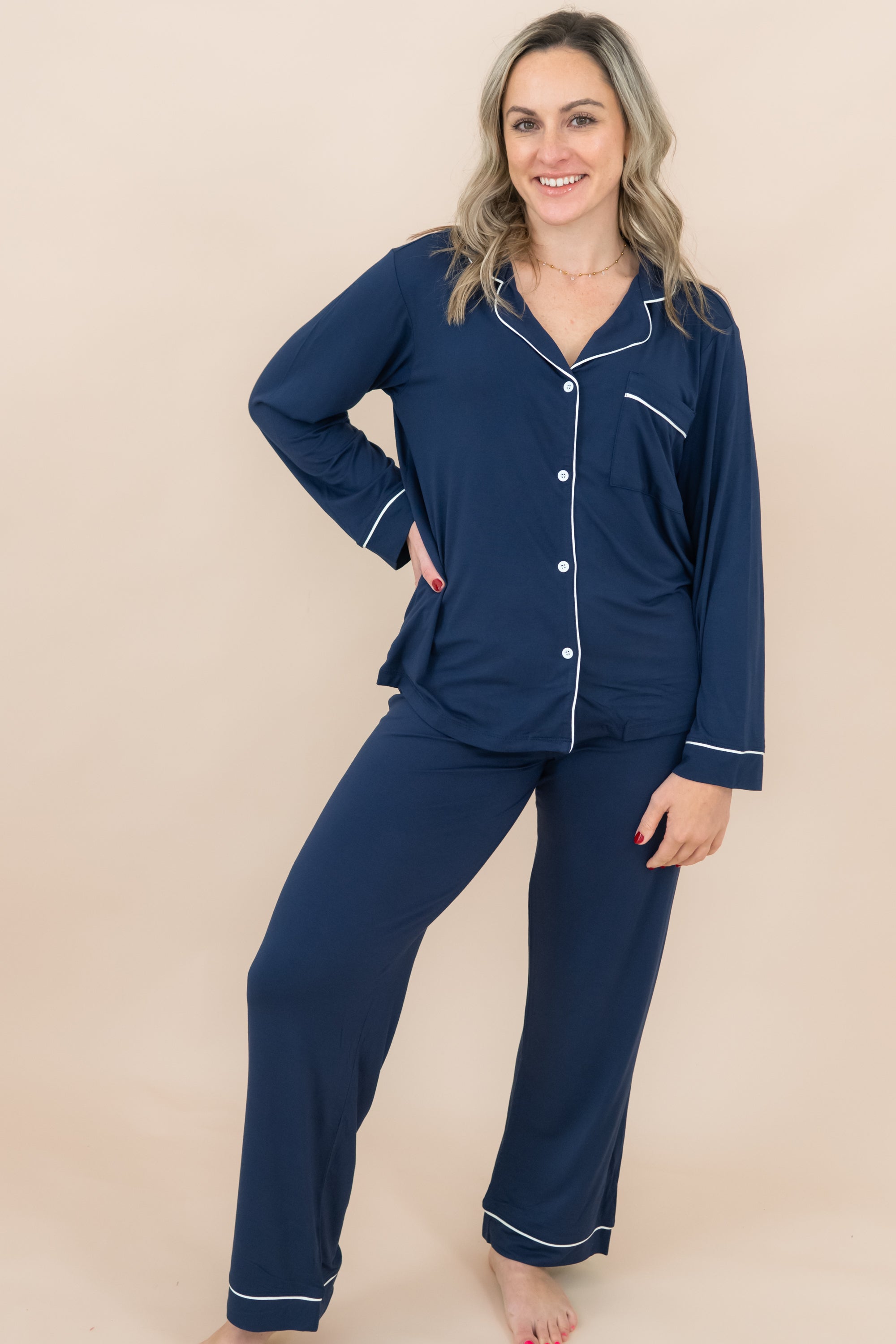 Woman wearing navy blue pajamas with white piping on a beige background