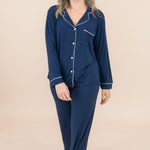 Woman wearing a navy blue pajama set with white buttons on a beige background