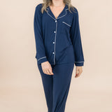 Woman wearing a navy blue pajama set with white buttons on a beige background