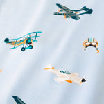 A repeating, all-over print featuring: a teal triplane with a light orange checker design; a racing seaplane colored in turquoise and light orange; a night fighter aircraft in teal with light orange accents; a white fighter bomber aircraft with a black nose, teal windows, and light orange accents; and a light grey aviator hat with goggles and blue stripes, over a sky blue background color called Breeze.