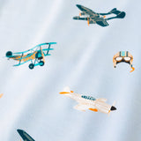 A repeating, all-over print featuring: a teal triplane with a light orange checker design; a racing seaplane colored in turquoise and light orange; a night fighter aircraft in teal with light orange accents; a white fighter bomber aircraft with a black nose, teal windows, and light orange accents; and a light grey aviator hat with goggles and blue stripes, over a sky blue background color called Breeze.