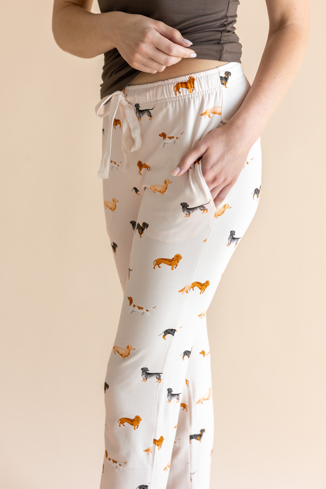Model showcasing the pockets of Women's Lounge Pants in Dachshund  under a brown camisole on a beige background
