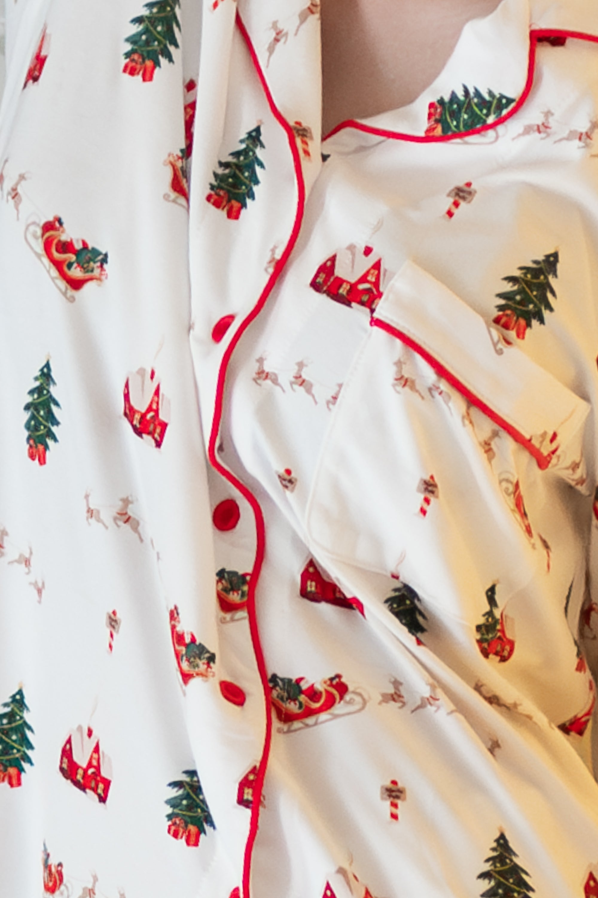 Close up of a white button up pajama top with red piping and a christmas pattern