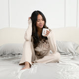 Female model sitting in bed on the Bamboo Sateen Sheet Set in Dove Gray holding a cup of coffee