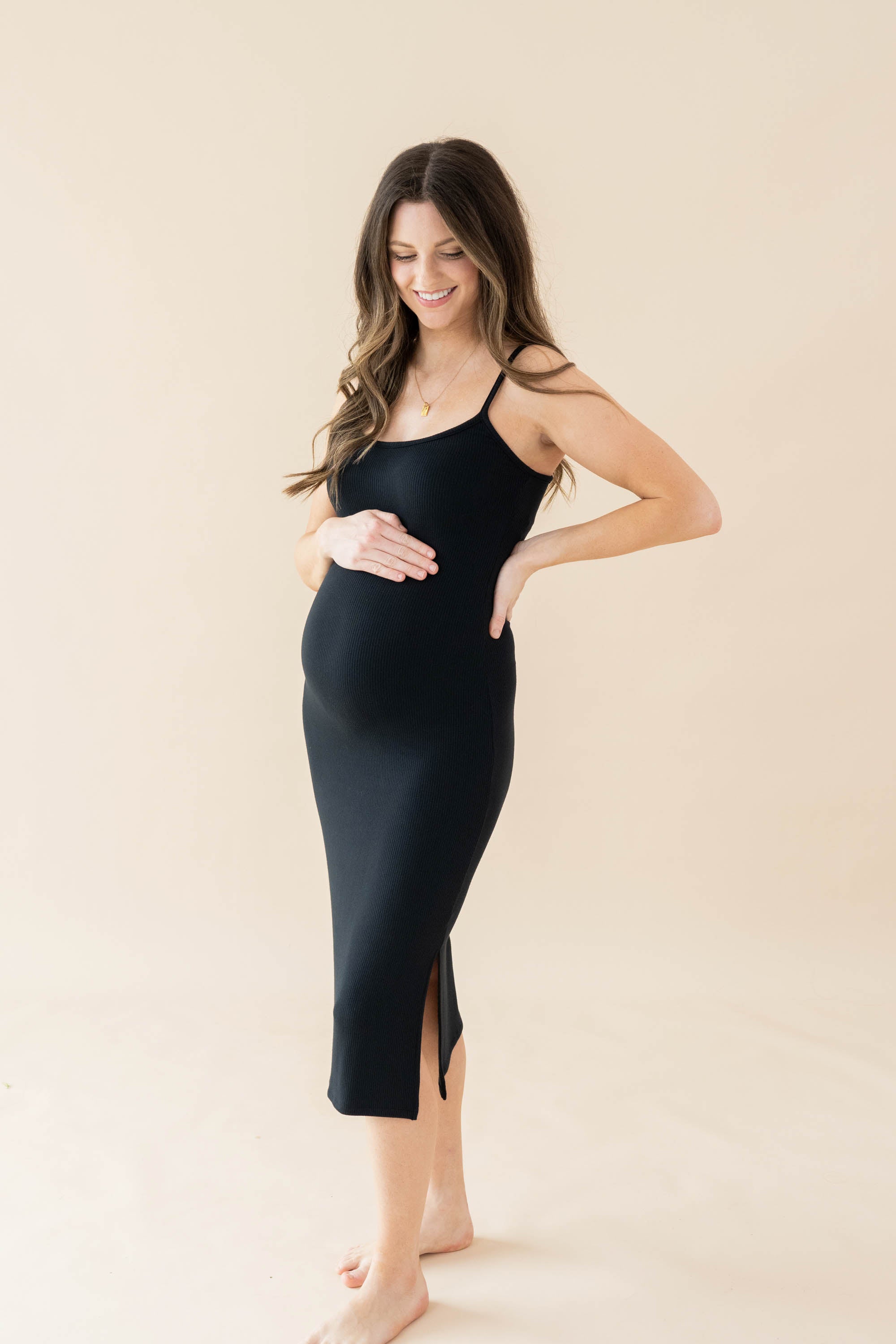Expectant mother wearing the Women's Ribbed Cami Dress in Midnight with one hand on top of her baby bump