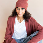 Modal wearing Chunky Knit Adult Pom in ember over white t-shirt and chunky knit women's cardigan in ember and blue jeans on a beige background