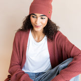 Modal wearing Chunky Knit Adult Pom in ember over white t-shirt and chunky knit women's cardigan in ember and blue jeans on a beige background