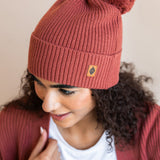 Modal wearing Chunky Knit Adult Pom in ember over white t-shirt and chunky knit women's  cardigan in ember on a beige background
