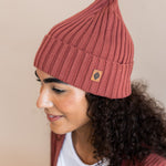 Modal wearing Chunky Knit Adult Ribbed Beanie in ember over white t-shirt and chunky knit women's cardigan in ember on a beige background