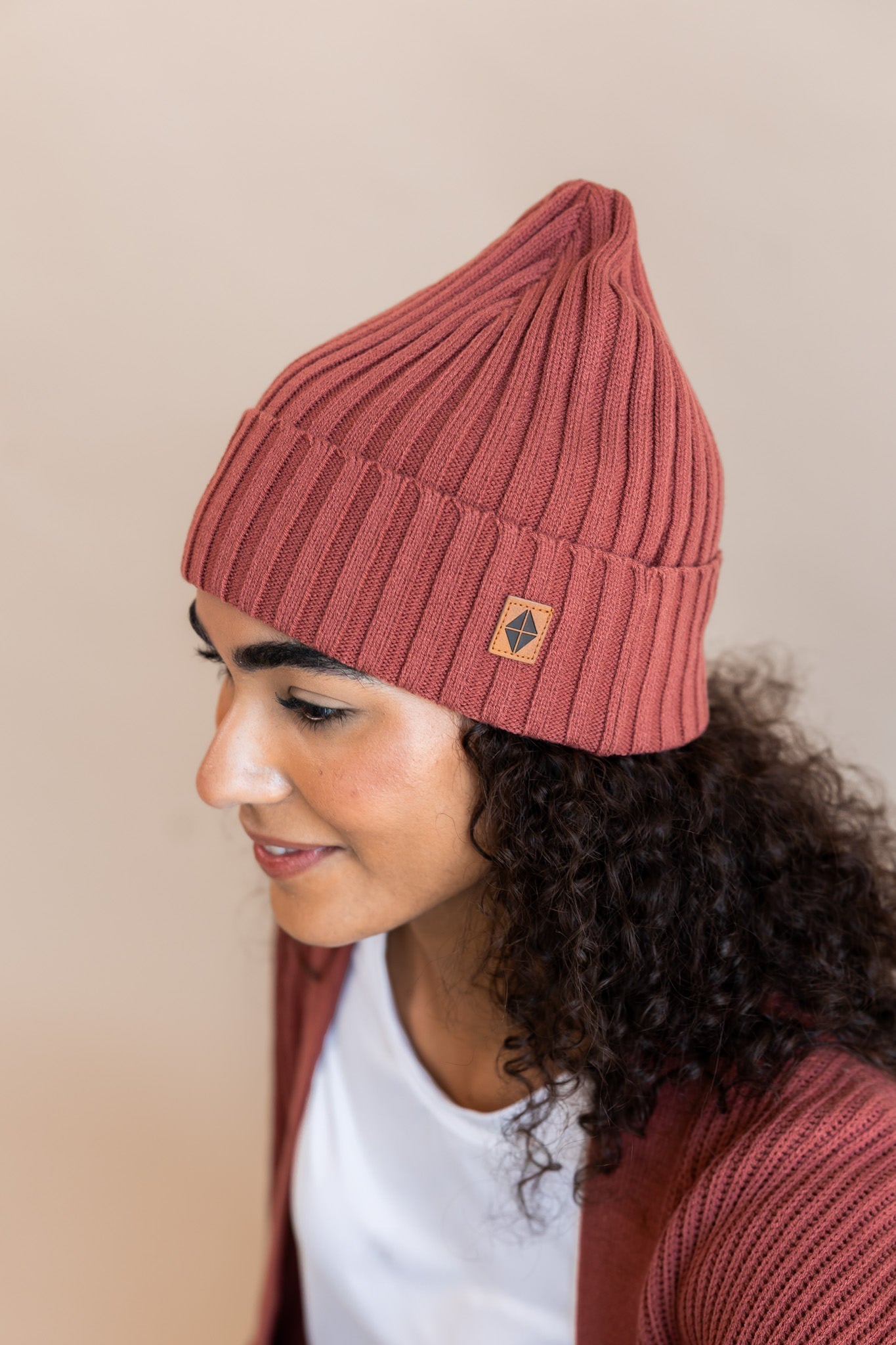 Modal wearing Chunky Knit Adult Ribbed Beanie in ember over white t-shirt and chunky knit women's cardigan in ember on a beige background