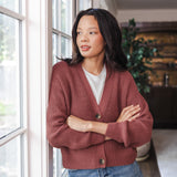 Woman leaned against the wall looking out the window wearing a cropped cardigan in ember
::: Model is 5'10" wearing size S ///