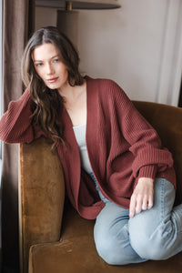 Woman leaning on the chair armrest in jeans and an oversized cardigan in ember