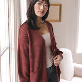 Modal standing near a window wearing Chunky Knit Women's Waffle Cardigan in Ember over white camisole and blue jeans
::: Model is 5'9" wearing size S ///