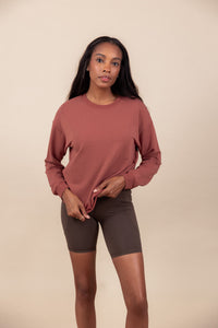 Woman tugging on her sweatshirt in ember and wearing biker shorts in espresso