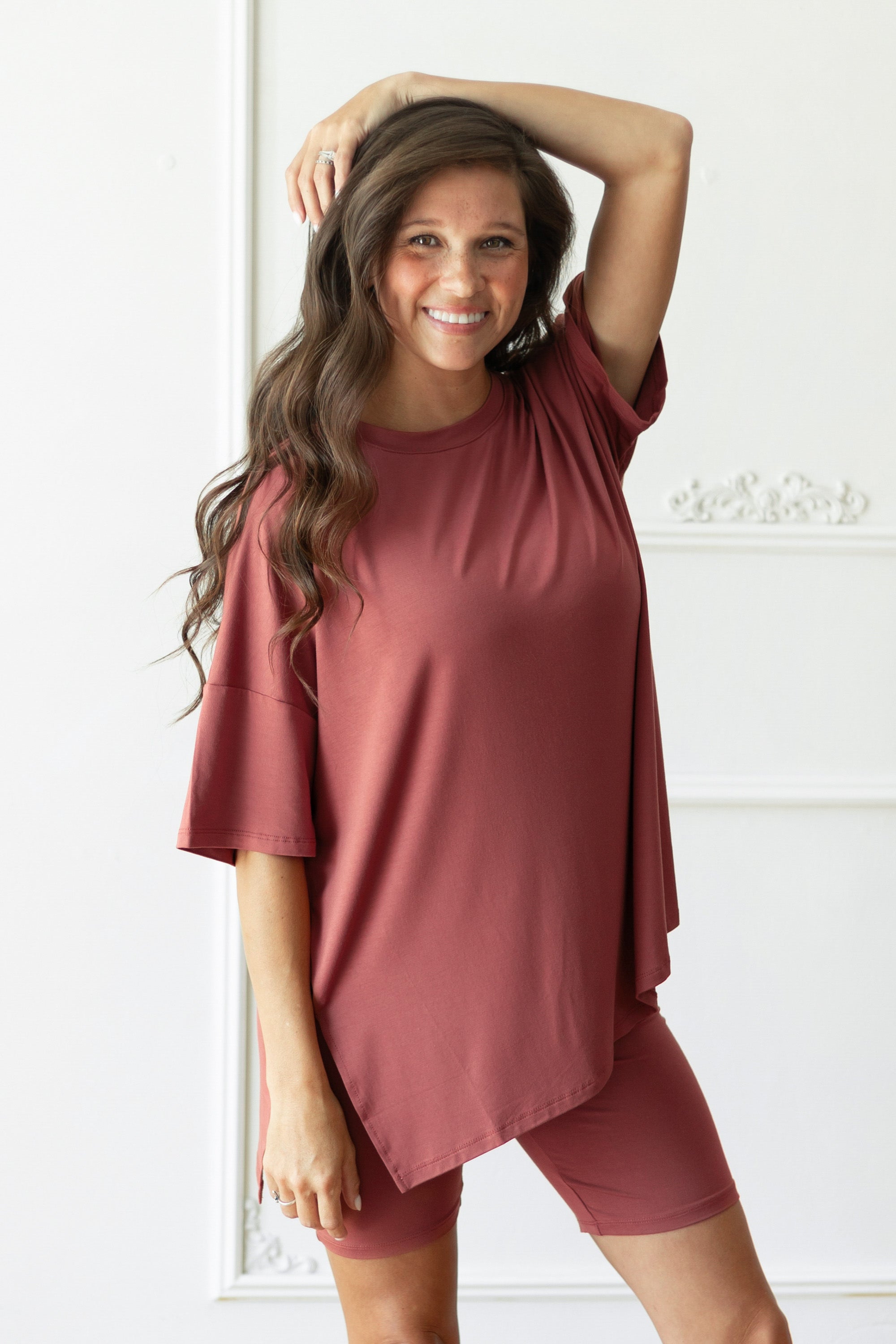 A woman modeling a matching dusty rose short-sleeve t-shirt and fitted biker shorts set against a white paneled wall.