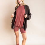 Model wearing Women’s Biker Short Set in Ember with Chunky Knit Oversized Cardigan in Espresso and Adult Socks in Ember on a beige background