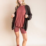 Model wearing Women’s Biker Short Set in Ember with Chunky Knit Oversized Cardigan in Espresso and Adult Socks in Ember on a beige background
