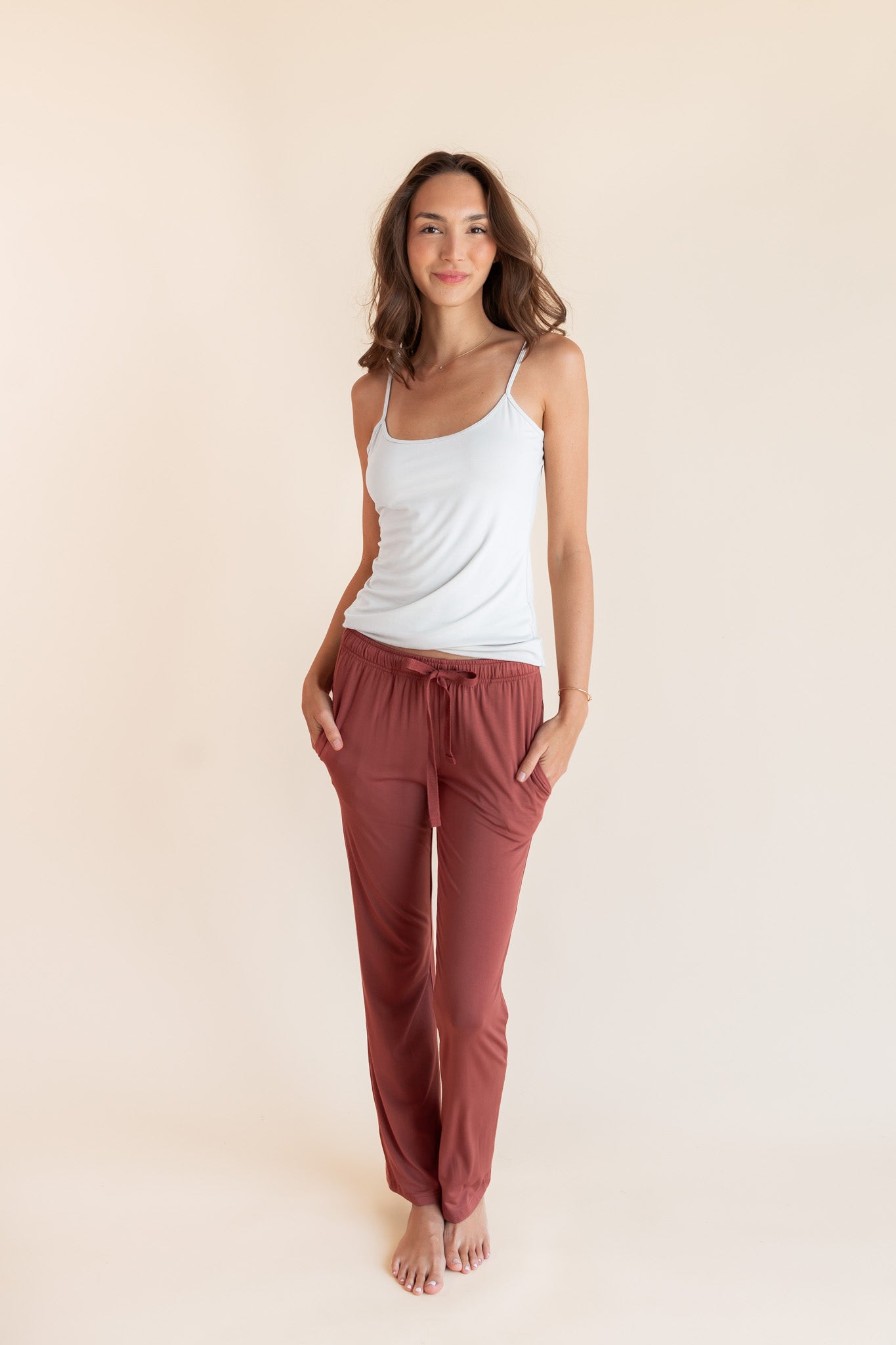 Model wearing Women's Lounge Pants in Ember with pockets under white camisole on a beige background
