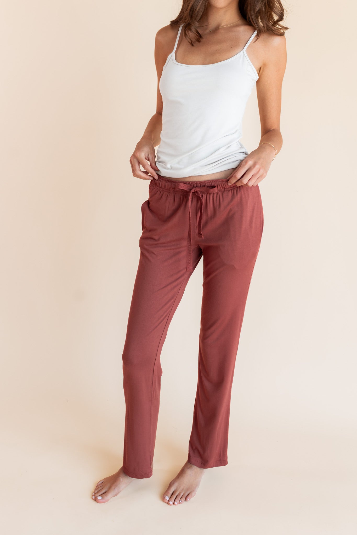 Model wearing Women's Lounge Pants in Ember under white camisole on a beige background