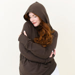 Woman with arms hugged around torso modeling the Kyte Women's French Terry Nursing Hoodie in Espresso 