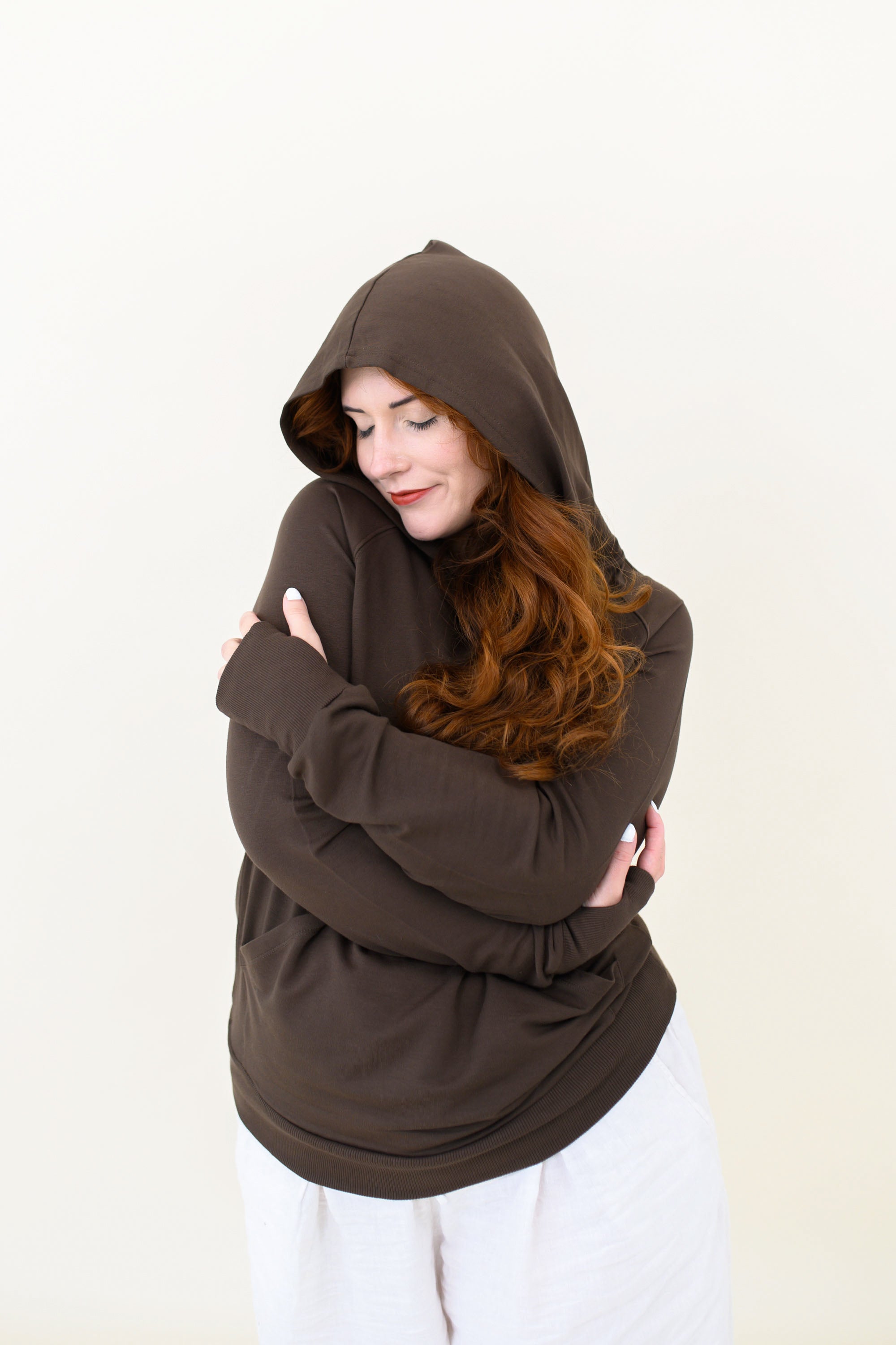 Woman with arms hugged around torso modeling the Kyte Women's French Terry Nursing Hoodie in Espresso 