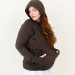 Smiling female wearing the Women's French Terry Nursing Hoodie in Espresso with the hood up and her hands in the kangaroo pocket