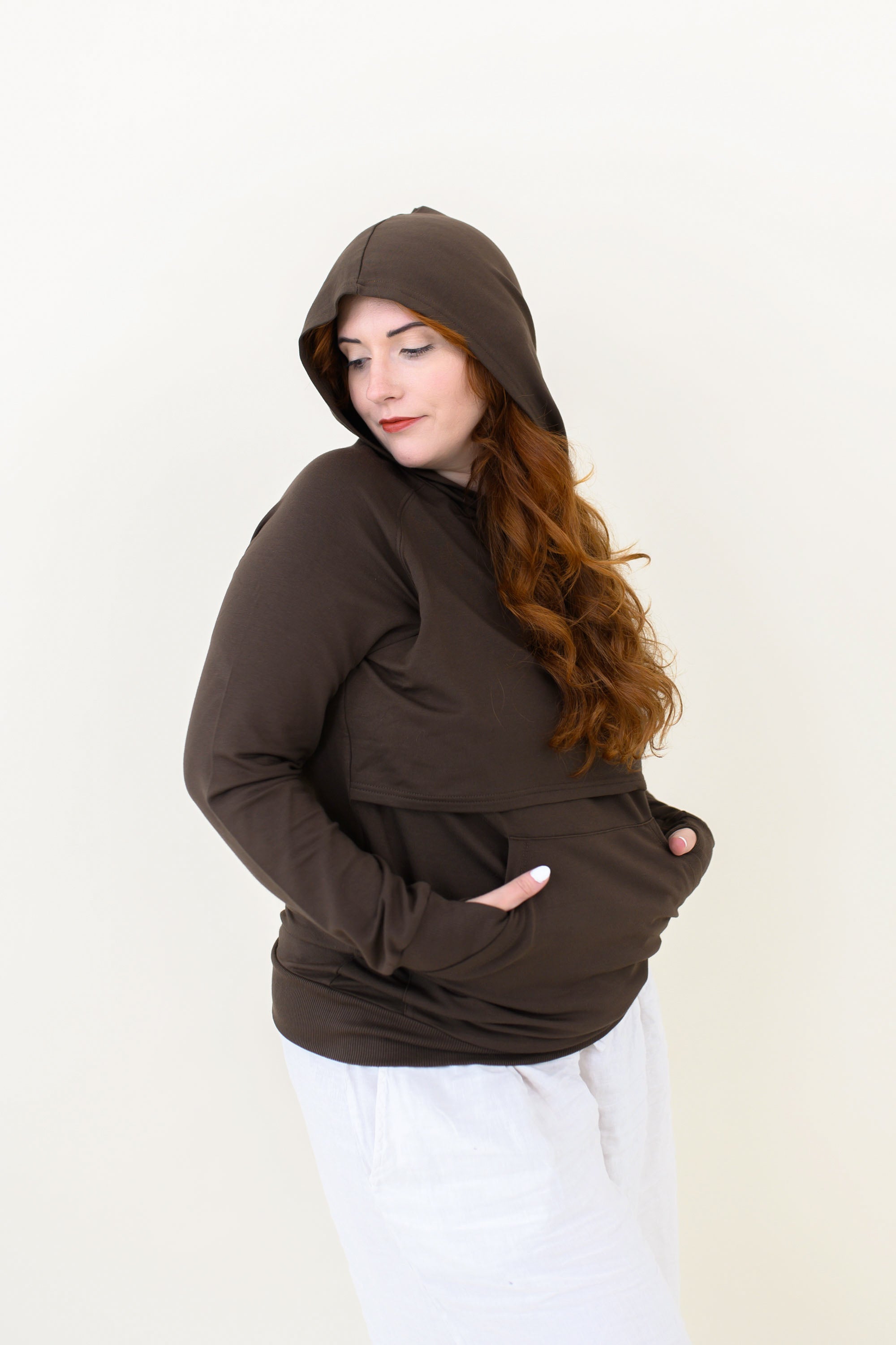 Smiling female wearing the Women's French Terry Nursing Hoodie in Espresso with the hood up and her hands in the kangaroo pocket