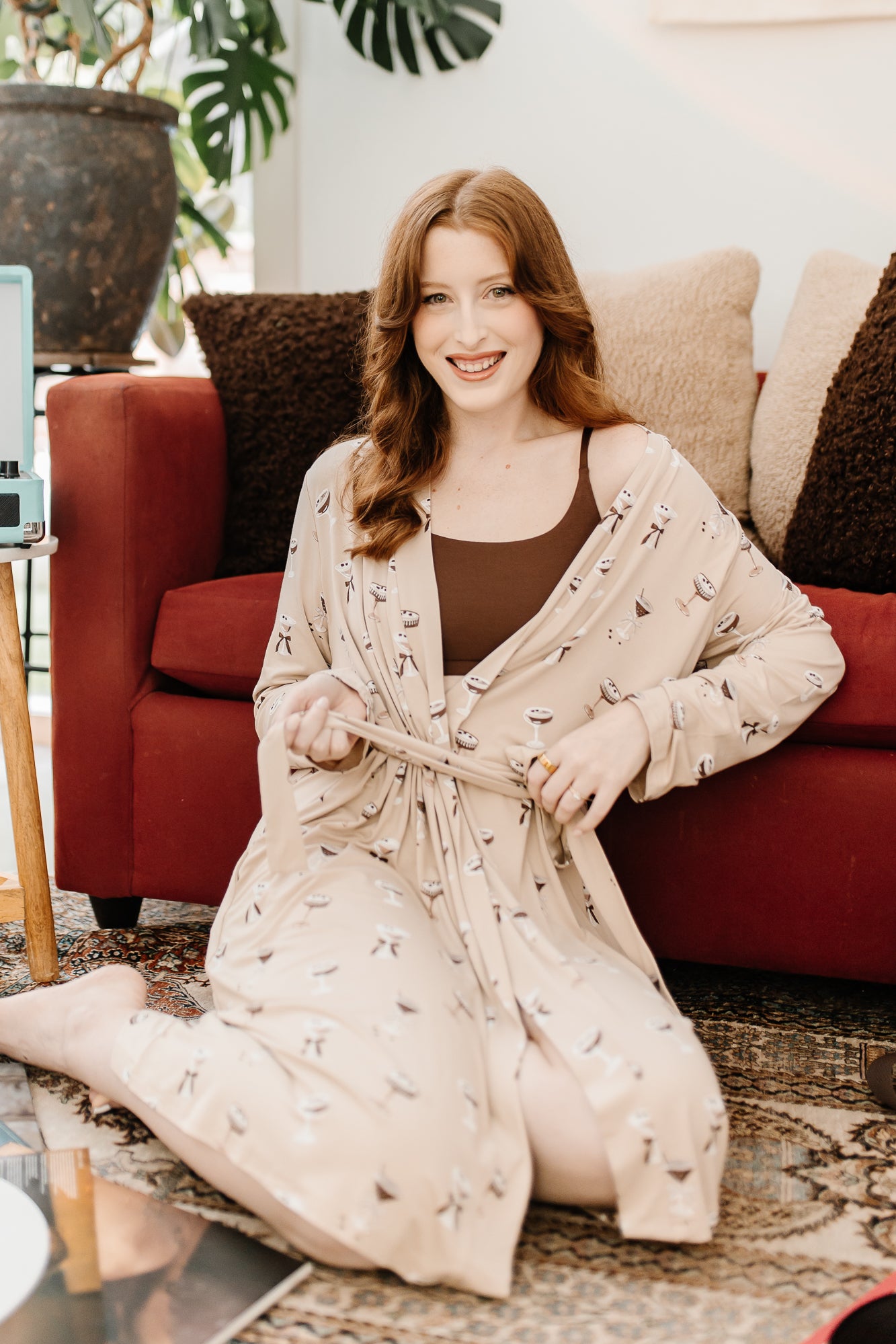 Smiling sitting woman sitting on the floor modeling the Kyte Women's Lounge Robe in Espresso Martini