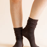 A close-up of a person's legs wearing dark brown ribbed crew socks against a solid light beige background.