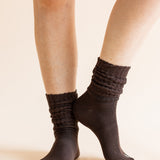 A close-up of a person's legs wearing dark brown ribbed crew socks against a solid light beige background.