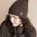 Modal wearing Chunky Knit Adult Pom in espresso over white t-shirt and chunky knit women's cardigan in espresso on a beige background