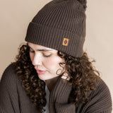 Modal wearing Chunky Knit Adult Pom in espresso over white t-shirt and chunky knit women's cardigan in espresso on a beige background
