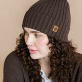 Modal wearing Chunky Knit Adult Ribbed Beanie in espresso over white t-shirt and chunky knit women's cardigan in espresso on a beige background