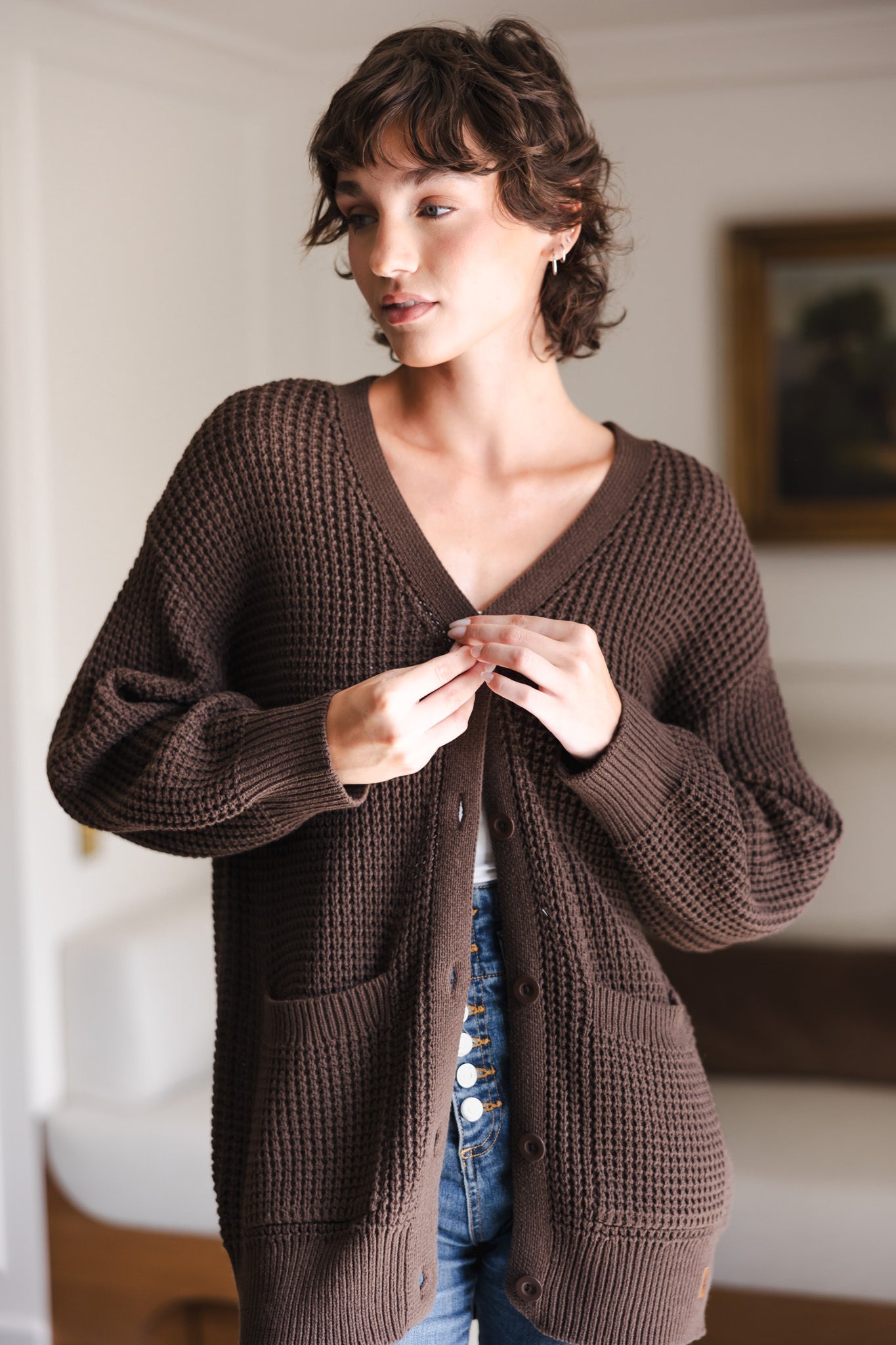 Modal buttoning Chunky Knit Women's Waffle Cardigan in Espresso over white camisole and blue jeans in a living room
