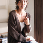 Modal sitting in a living room wearing Chunky Knit Women's Waffle Cardigan in Espresso over white camisole and blue jeans